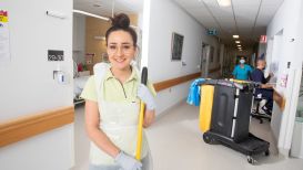 A cleaner in a hospital corridor holding a mop